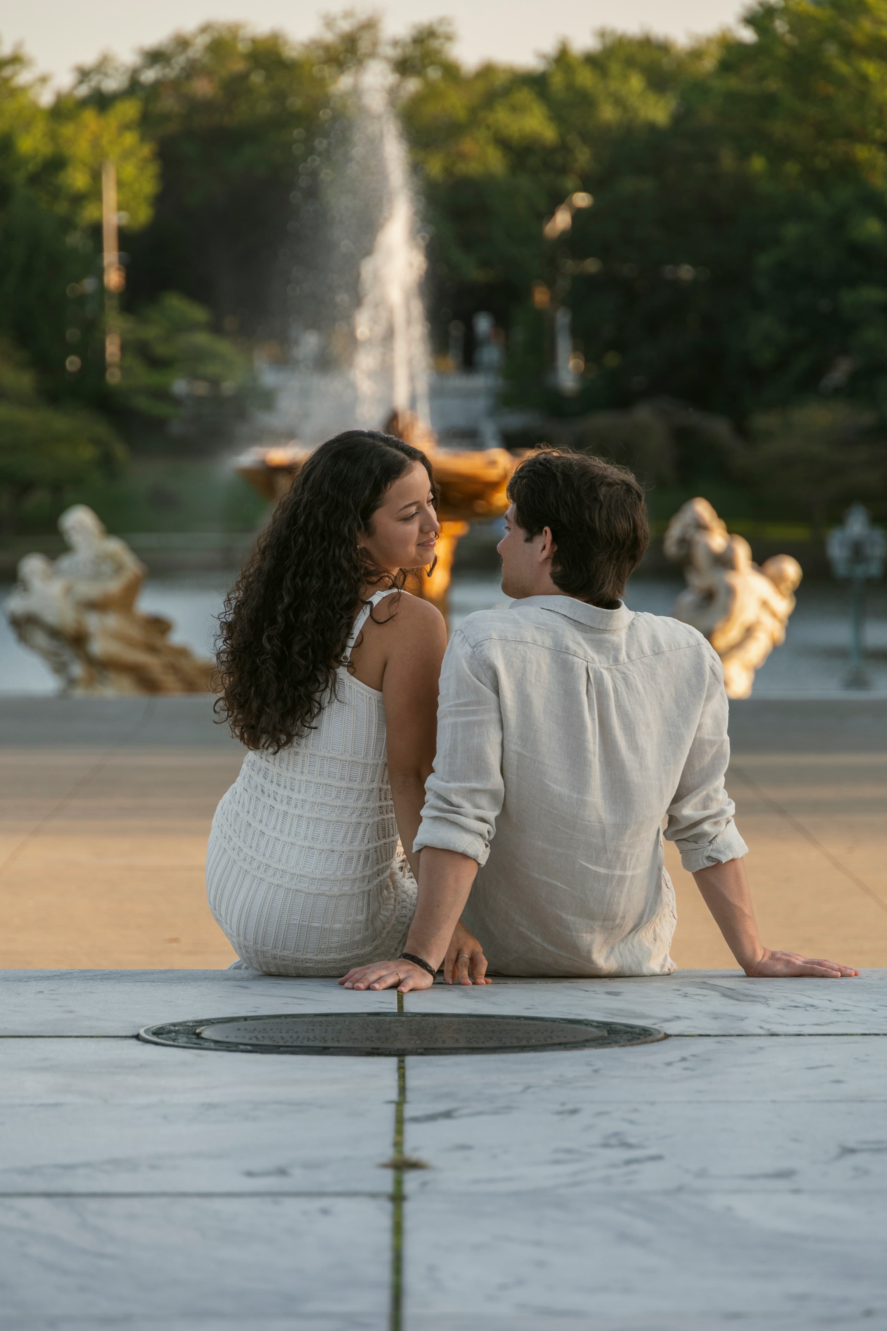 Couple sitting on marble steps in front of an ornate fountain