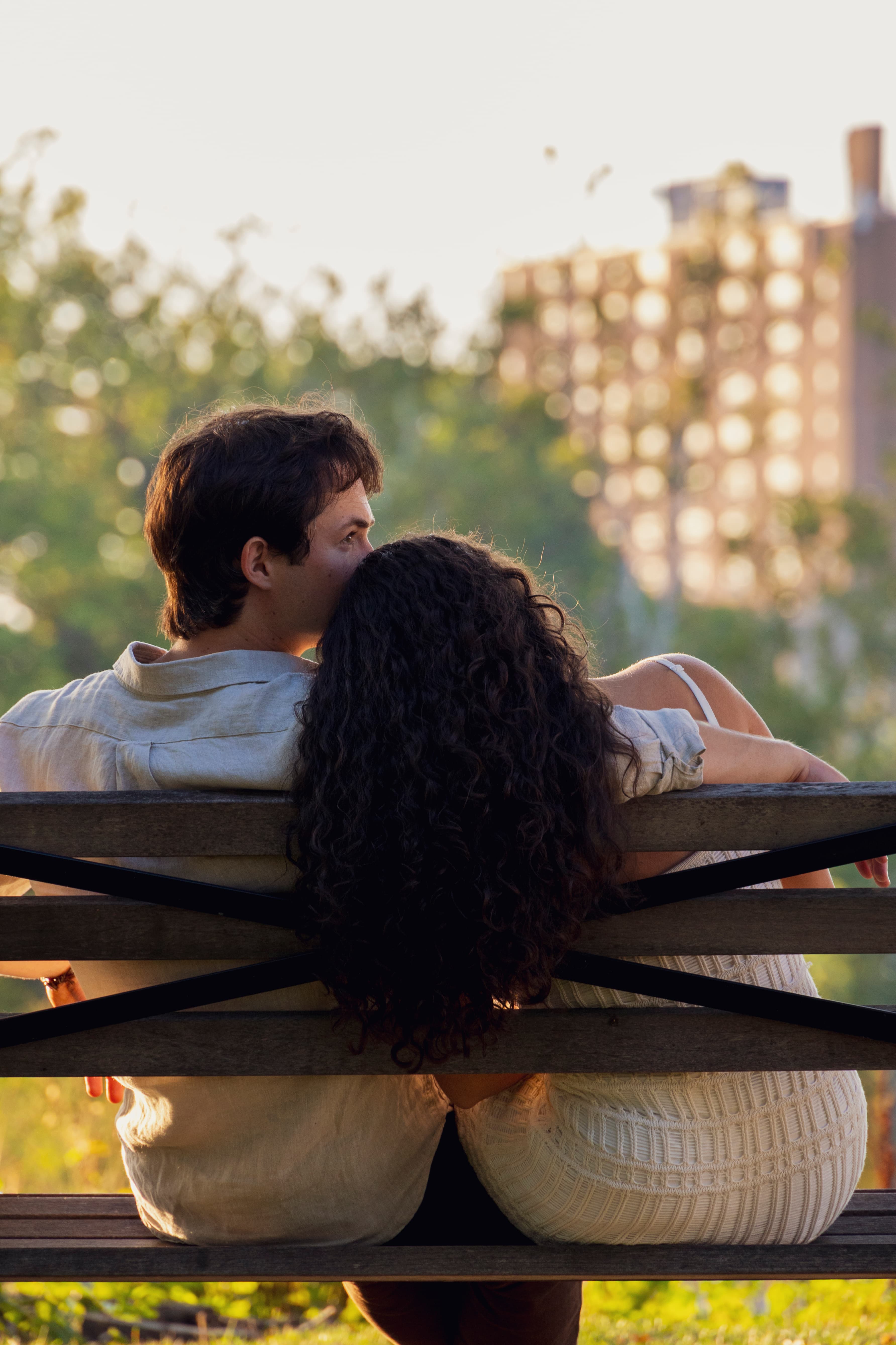 Couple on bench facing away, city skyline softly blurred behind