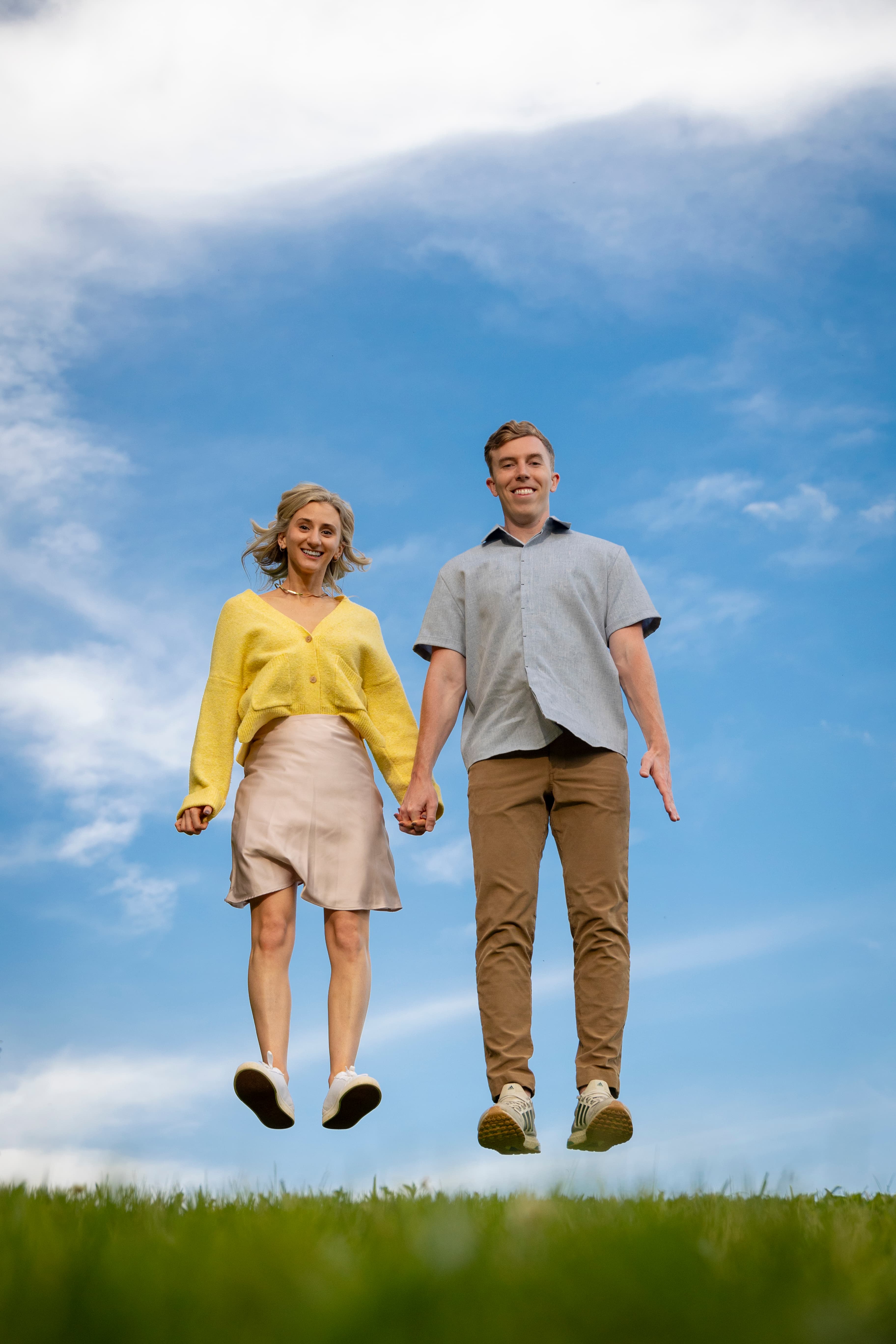 Couple holding hands jumping together against blue sky