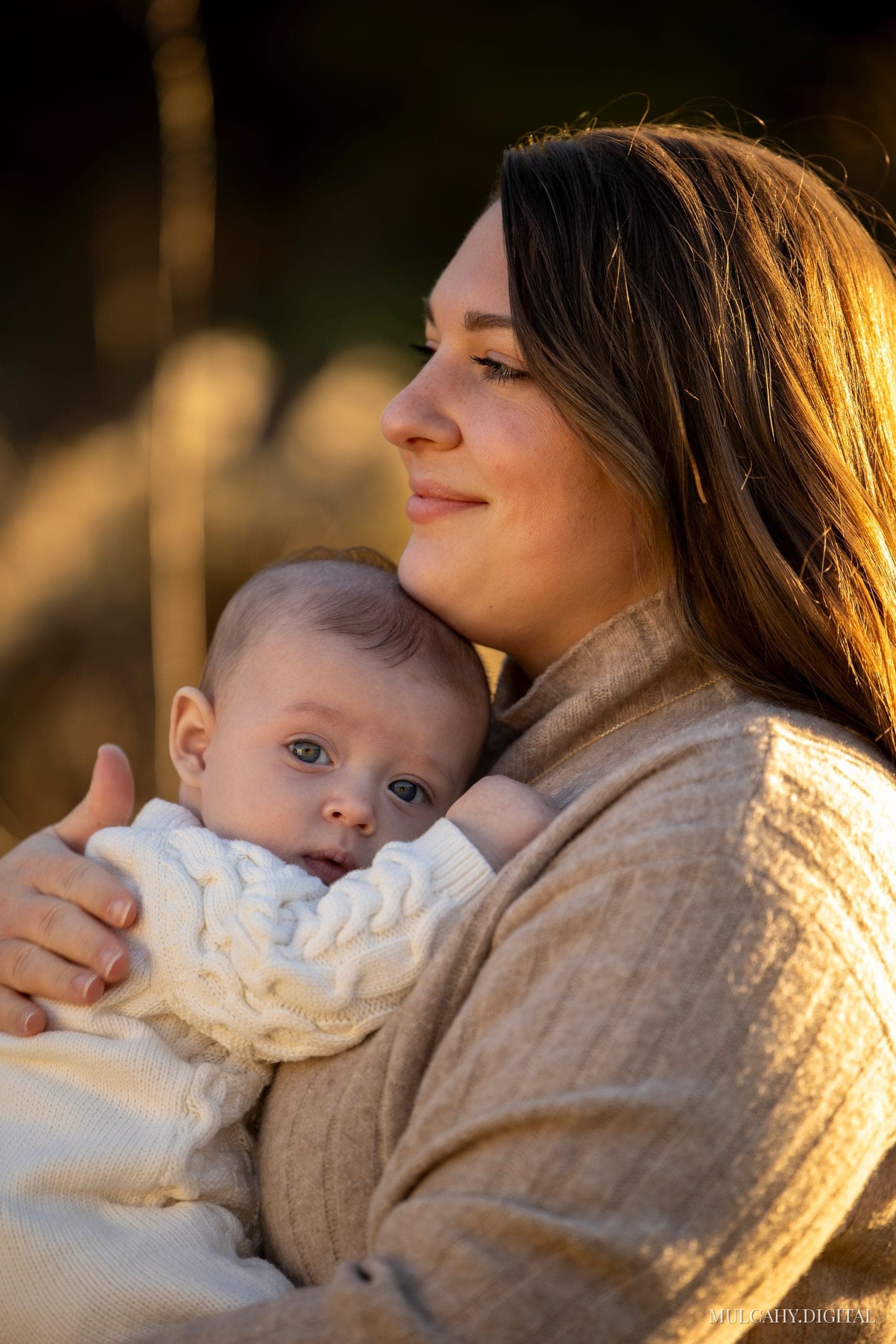 Mother cradling her baby against her shoulder in warm golden backlight