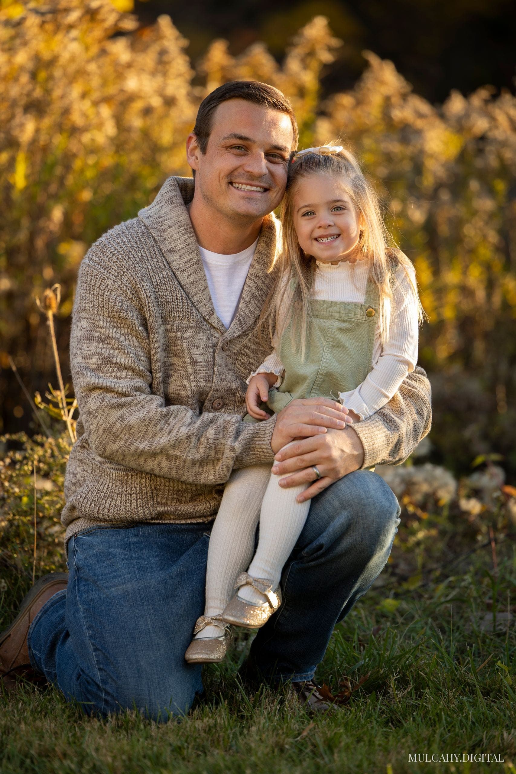 Father kneeling with his young daughter on his knee in a sunlit autumn field