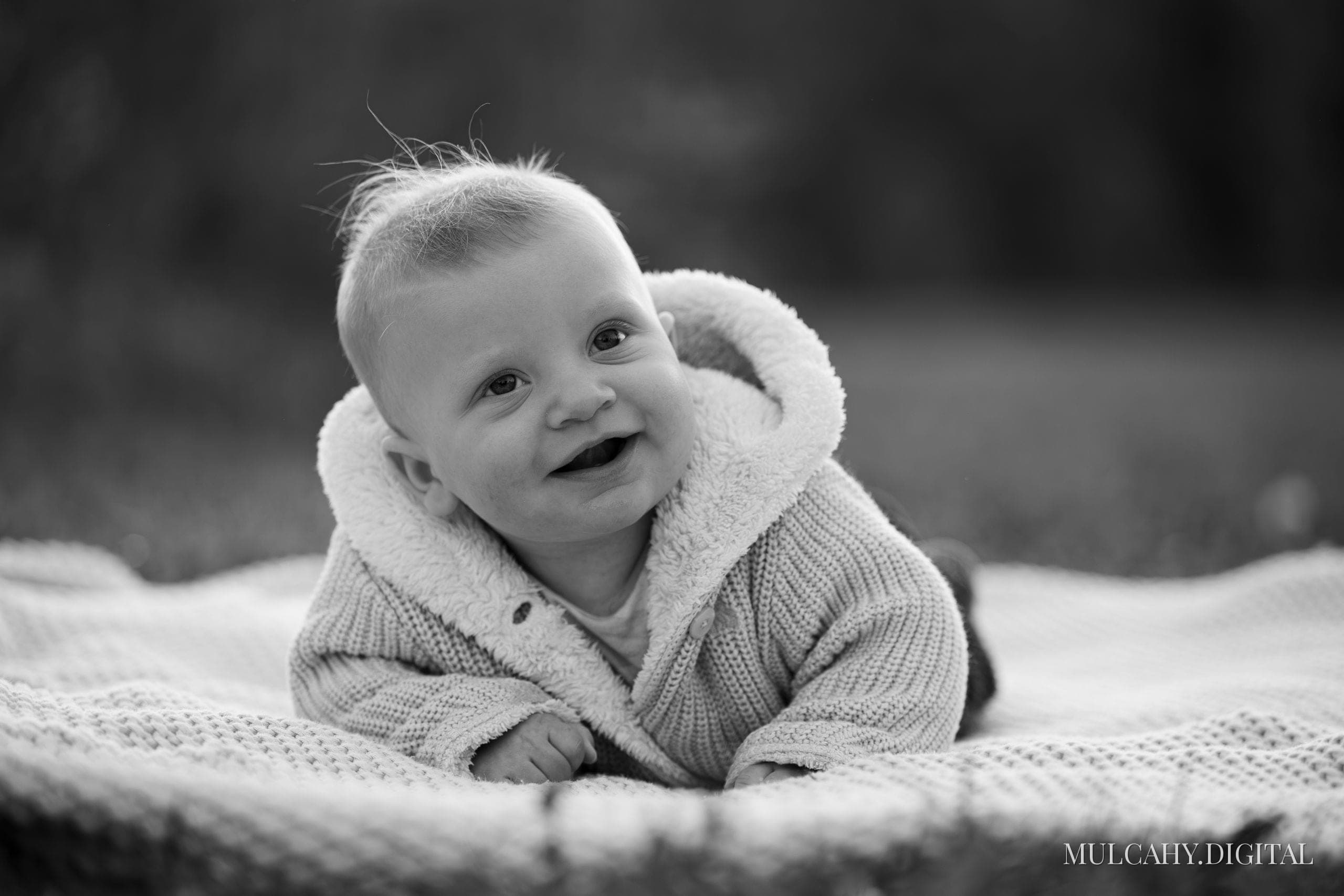 Black-and-white portrait of a smiling baby lying on a knit blanket