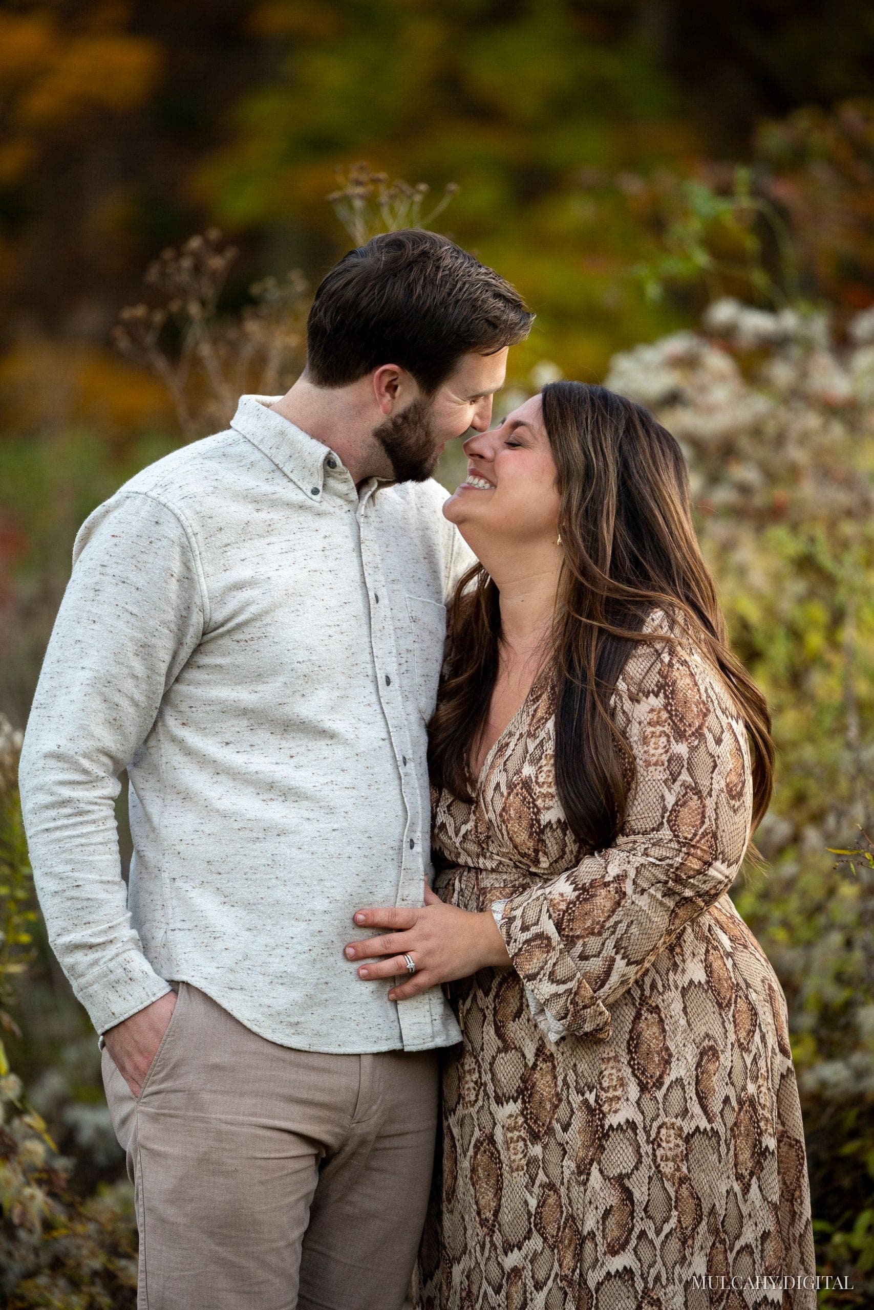 Couple touching foreheads and laughing among autumn brush, the woman in a patterned dress