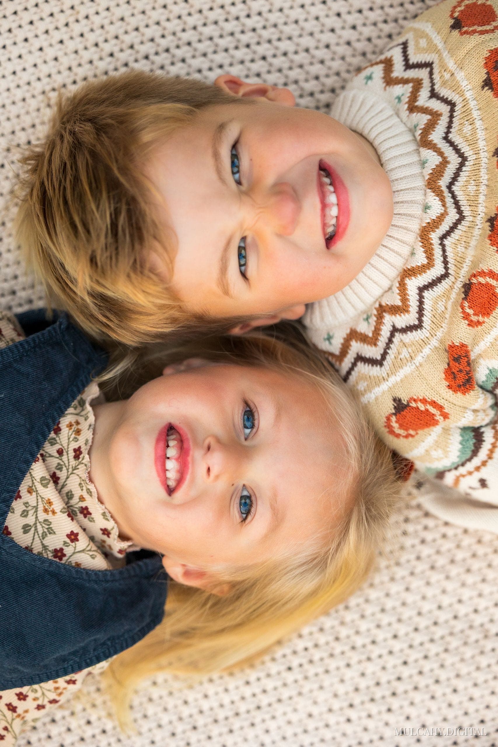 Overhead portrait of two blond siblings lying head to head, smiling up at the camera