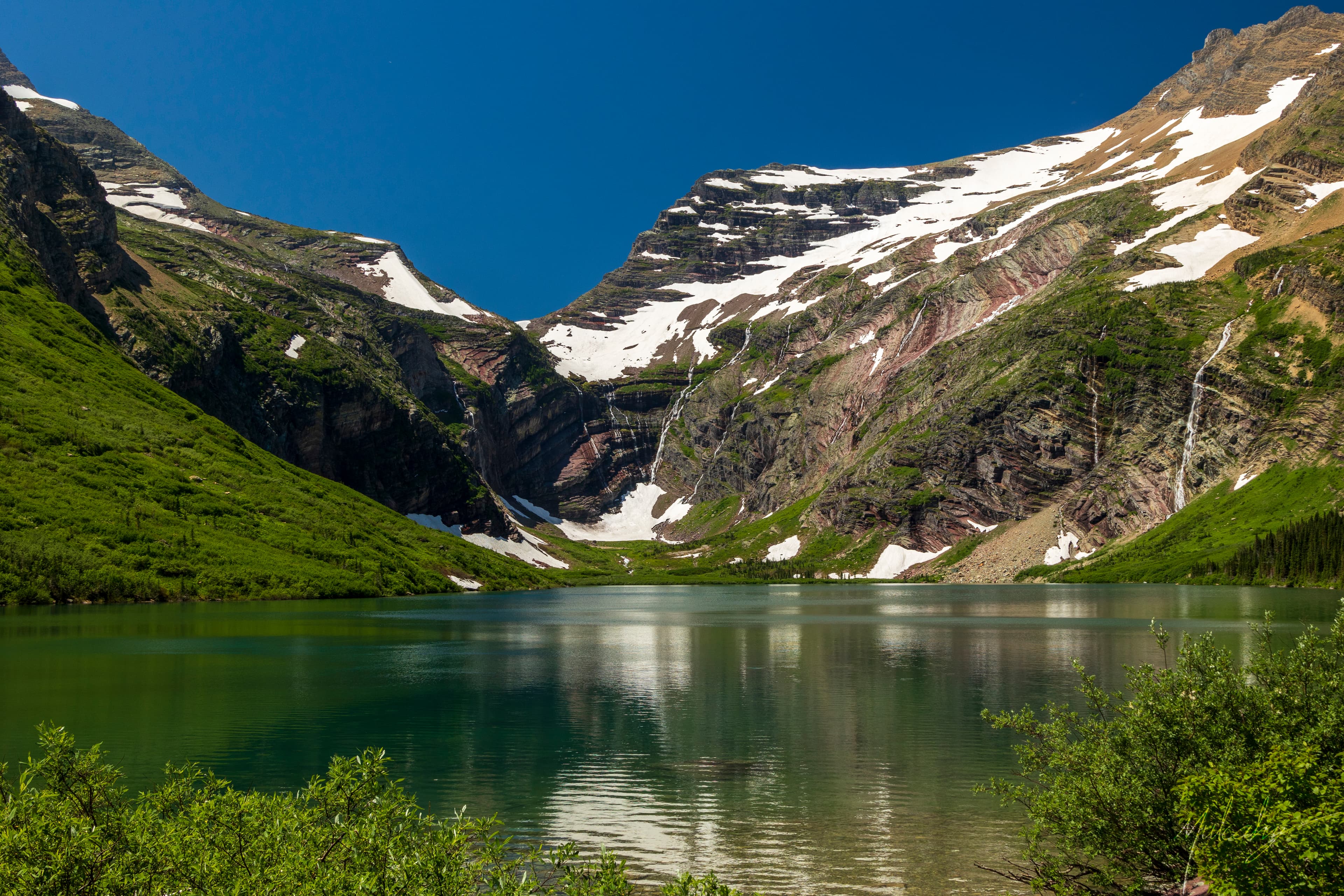 Glacial cirque lake surrounded by snow-patched peaks and waterfalls