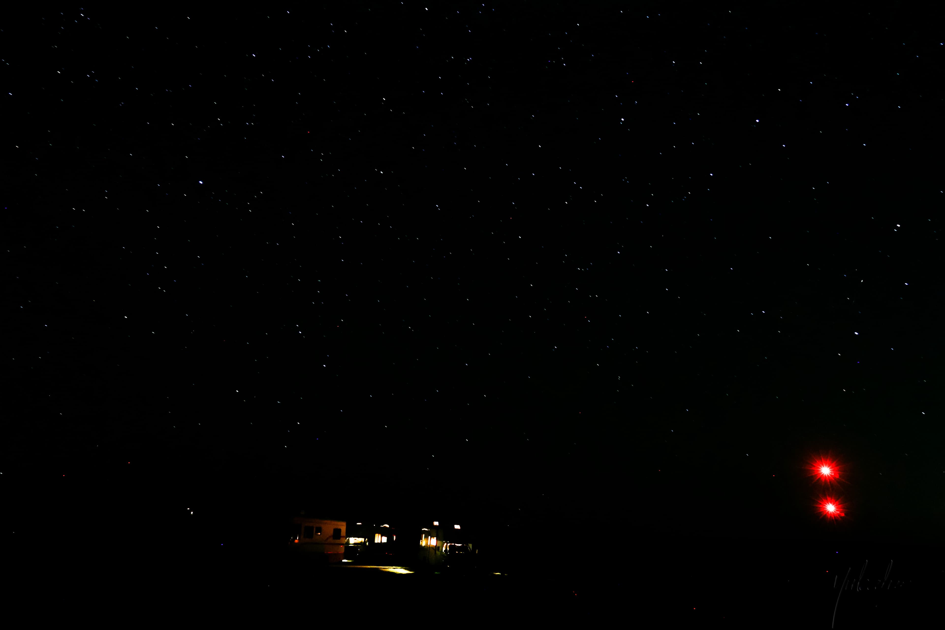 Dense starfield over a dark campsite, red aircraft warning lights