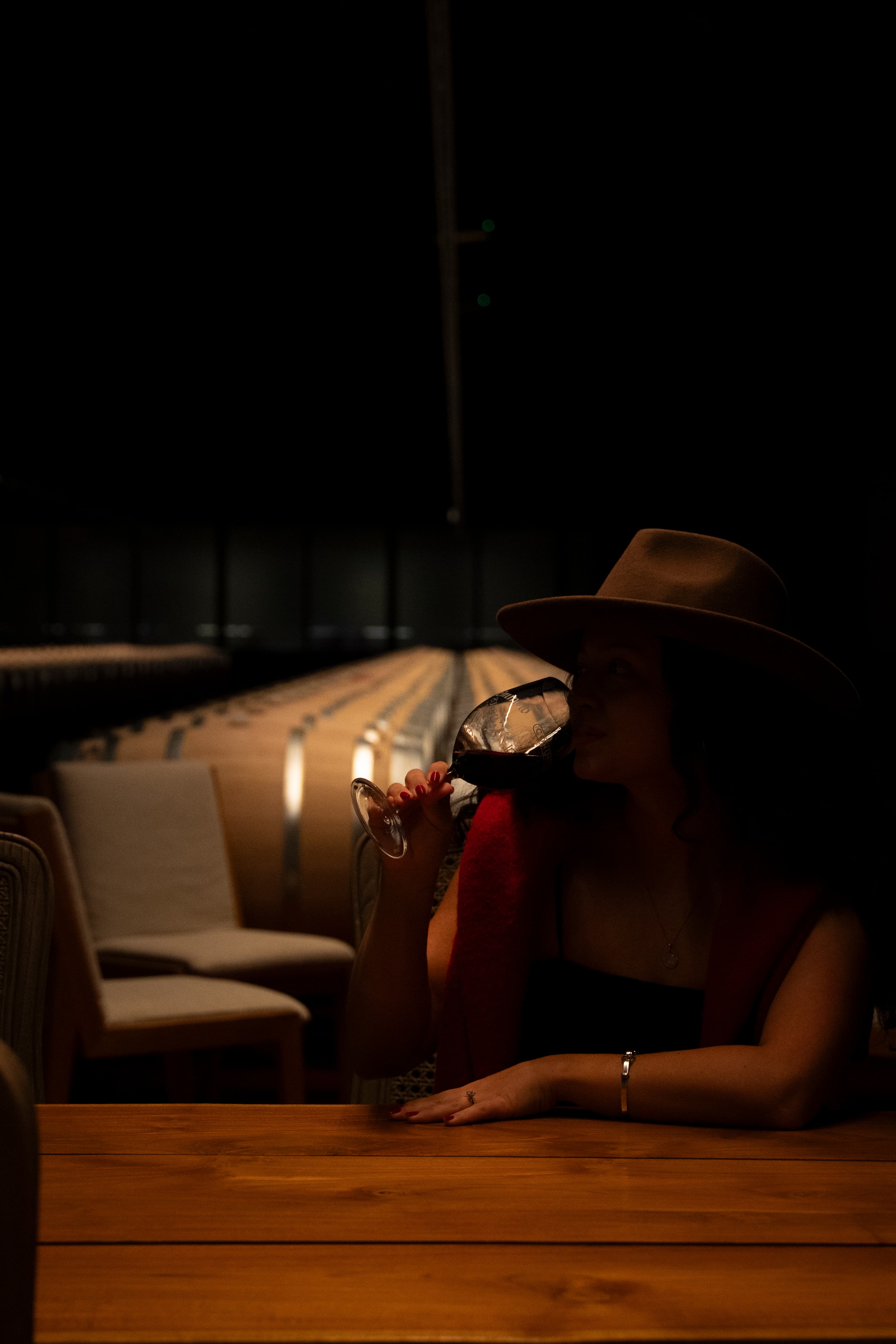 Woman in wide-brim hat sipping red wine in a dark winery tasting room