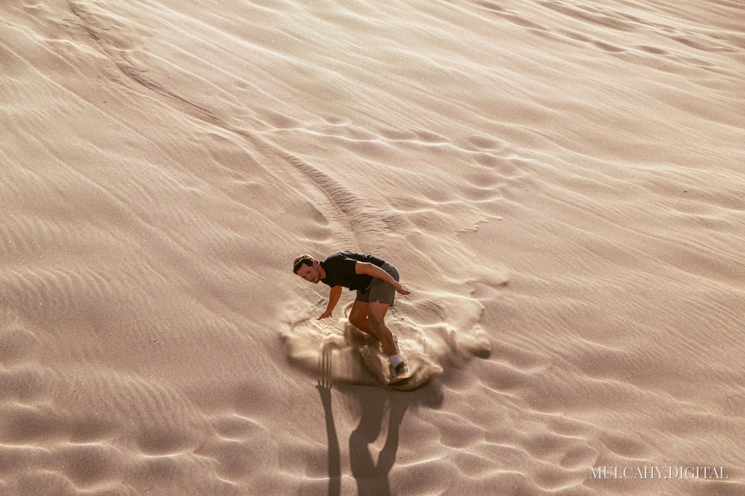 Man climbing a steep rippled sand dune in warm afternoon light