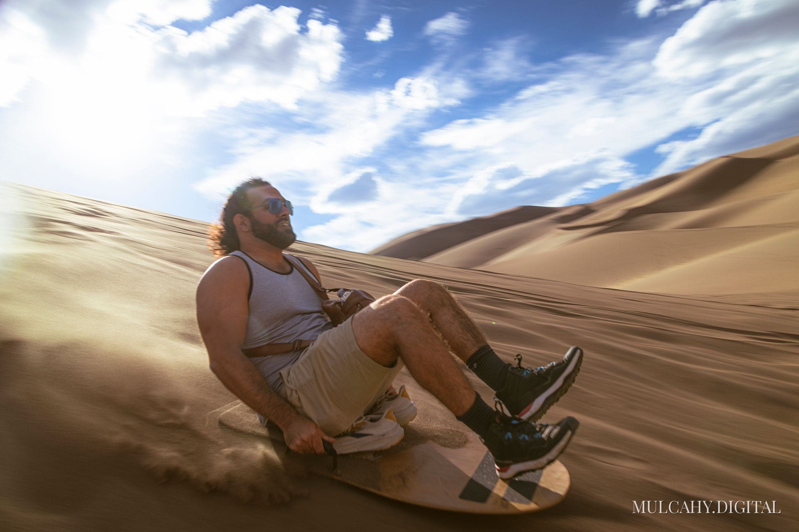 Man riding a sandboard down a tall dune with motion blur, sweeping dunes behind